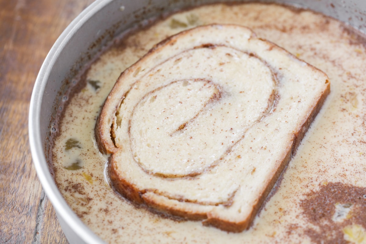 Dipping sliced bread in egg mixture for making cinnamon bread french toast.