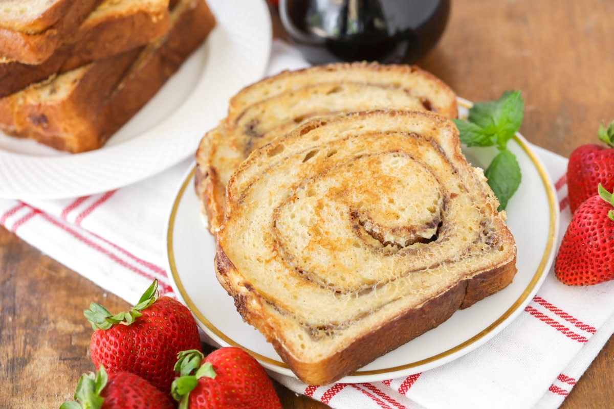 Two slices of cinnamon bread french toast served on a plate with fresh strawberries.