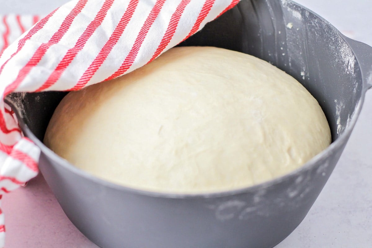 Homemade pizza dough rising in a grey bowl.