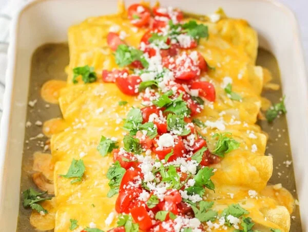 Honey lime chicken enchiladas rolled up and baked in white baking dish.