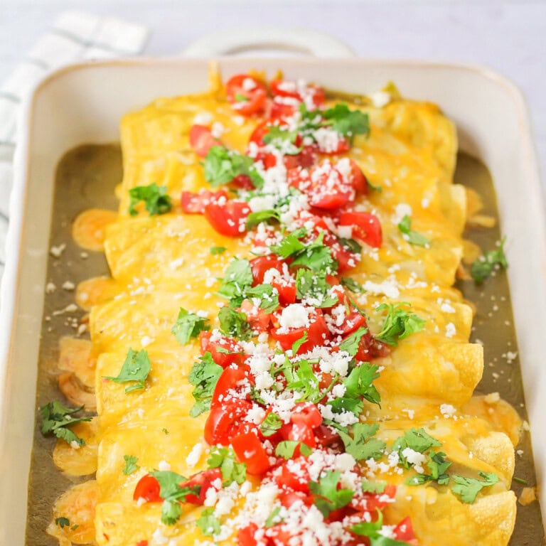 Honey lime chicken enchiladas rolled up and baked in white baking dish.