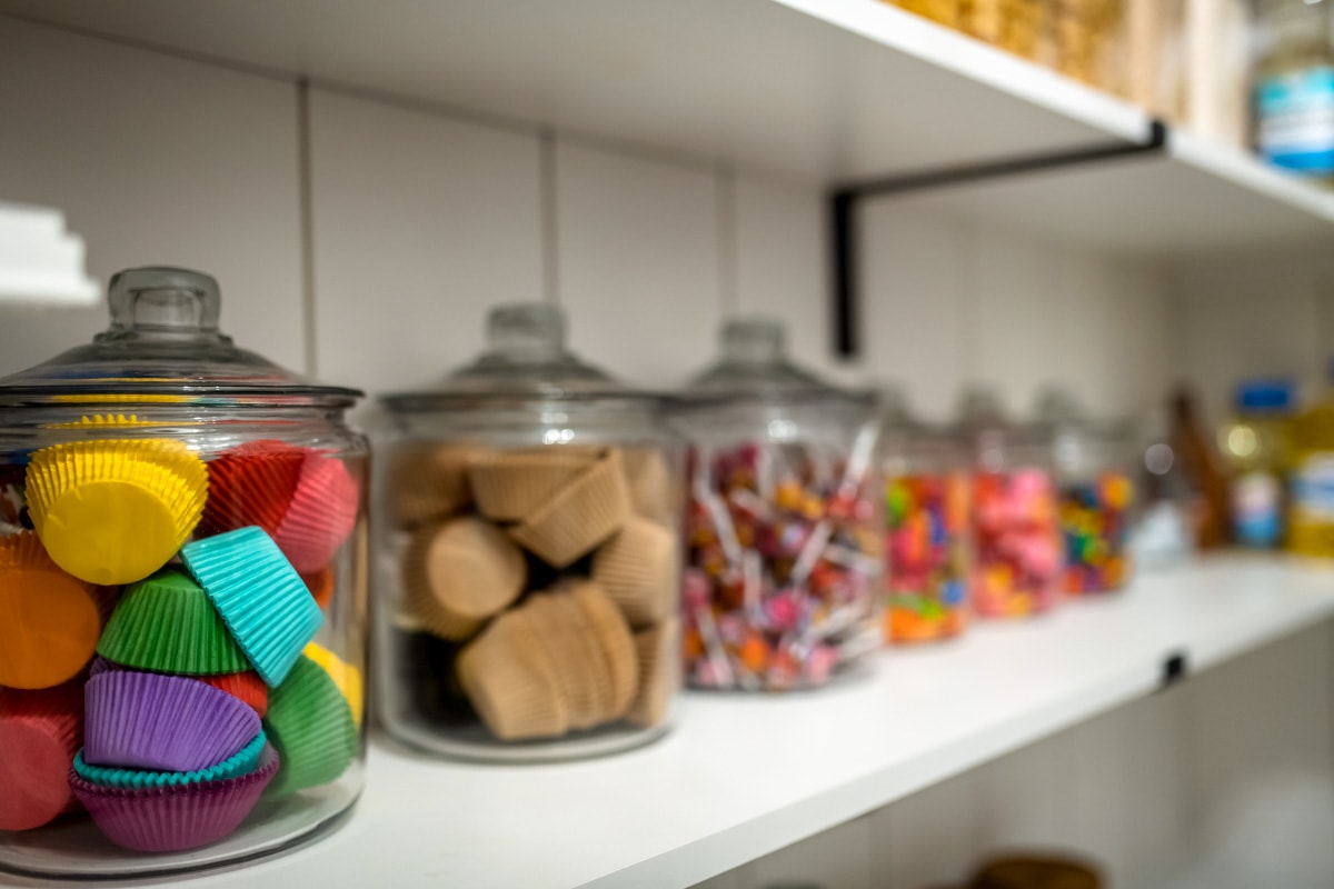 A pantry shelf with jars filled with cupcake liners and different types of candy.