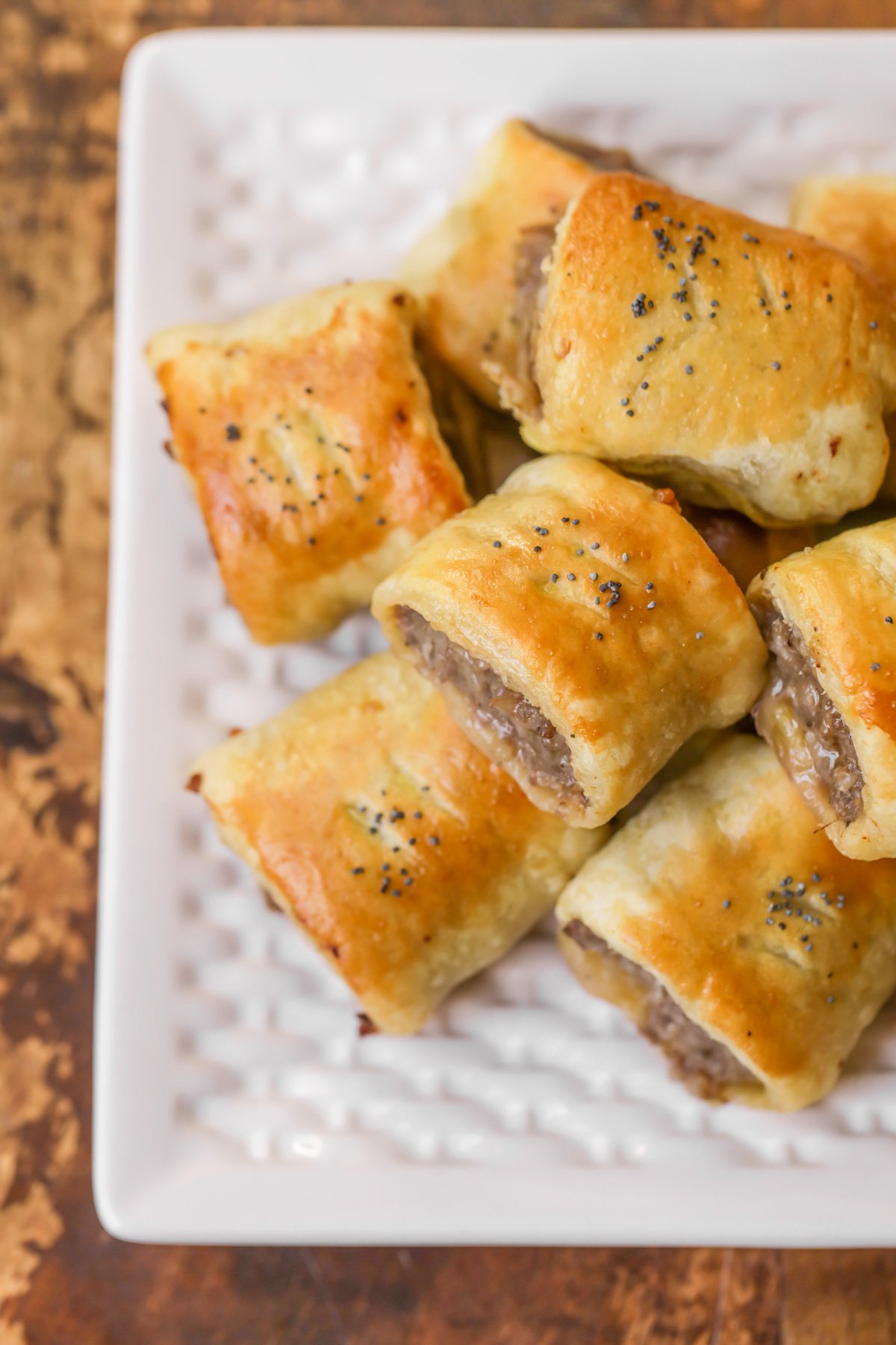 Puff pastry sausage rolls on white platter.