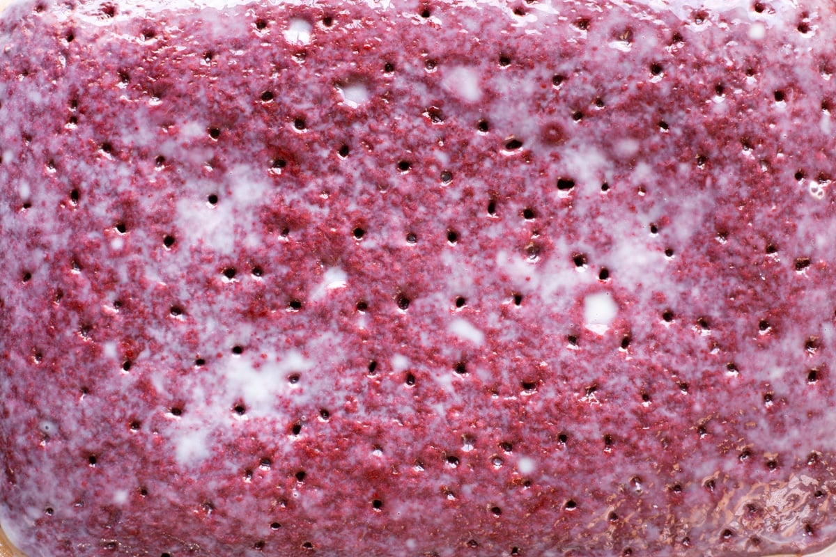 Unfrosted red velvet poke cake filled with poke holes.