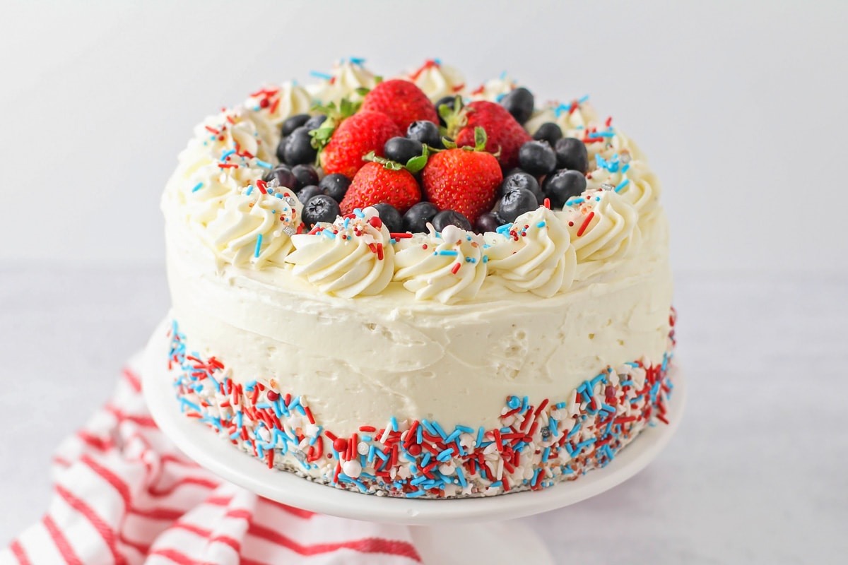 Make a spectacular red white and blue cake that's beautifully festive, delicious, and incredibly easy to put together! Red, white and blue cake with sprinkles and fruit perfect for any patriotic holiday.
