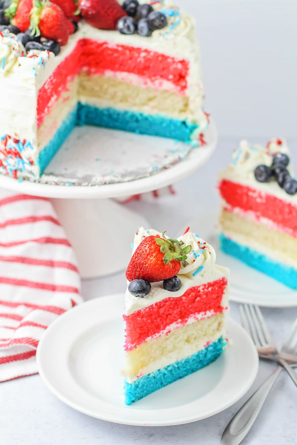 A slice of layered red white and blue cake topped with fresh berries.