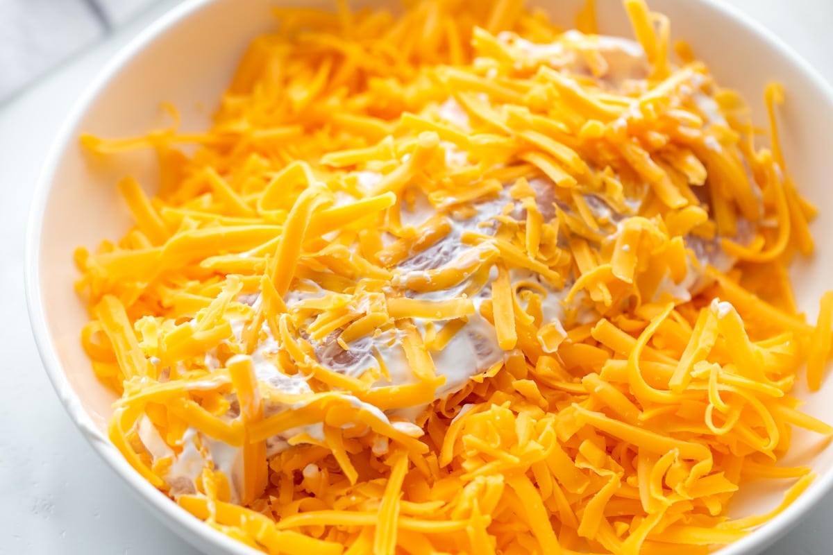 Chicken breast covered in shredded cheese in a white bowl.