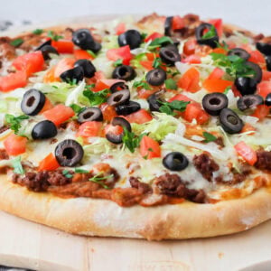 Homemade Taco pizza with toppings on cutting board.