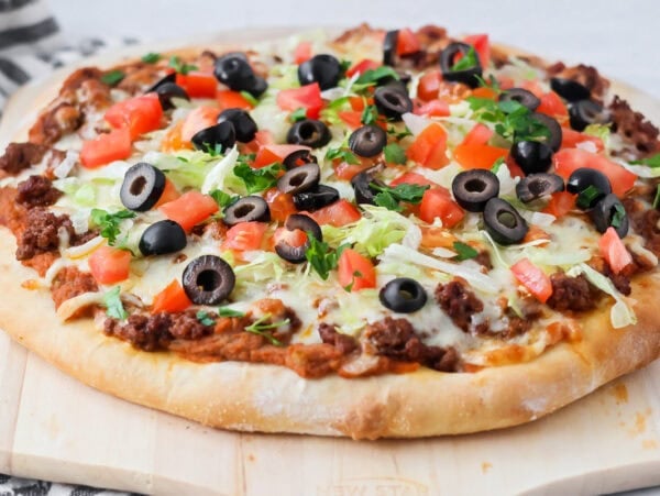 Homemade Taco pizza with toppings on cutting board.