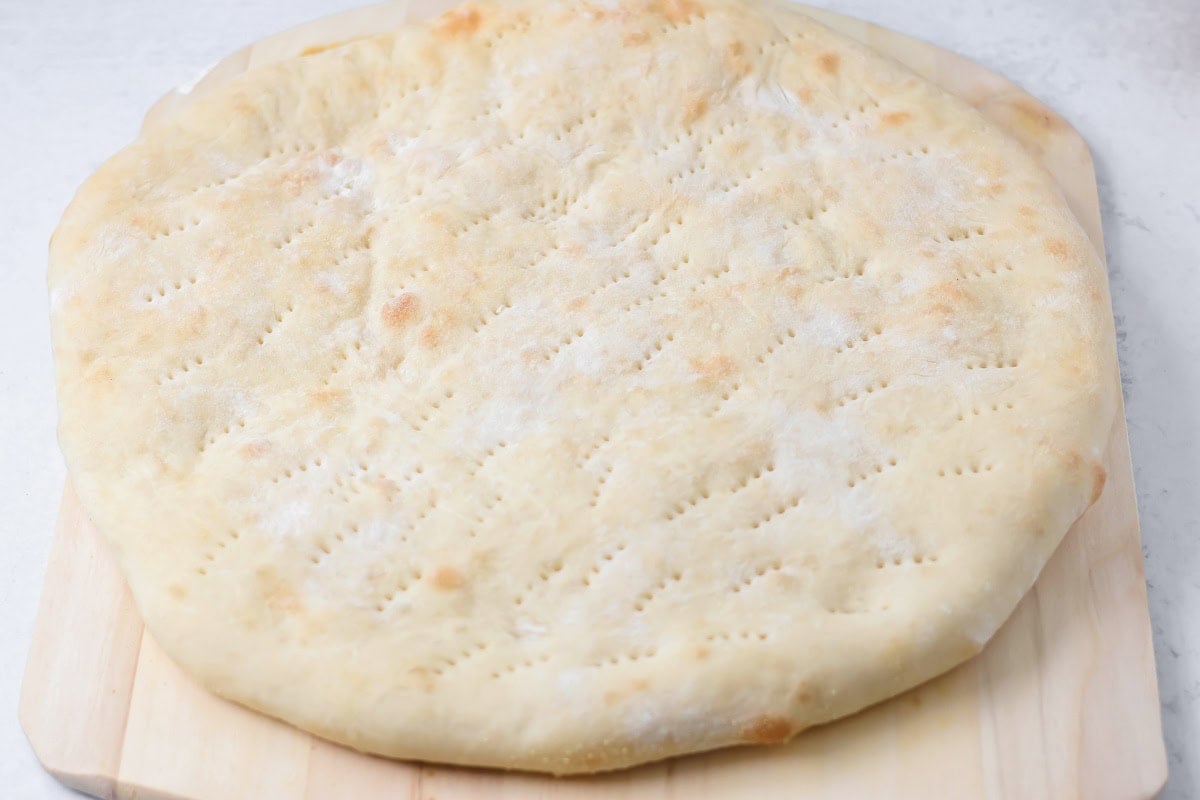 Pizza crust cooked on cutting board.