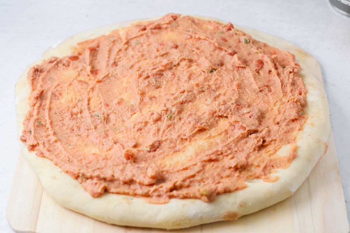 Pizza crust topped with beans on cutting board.