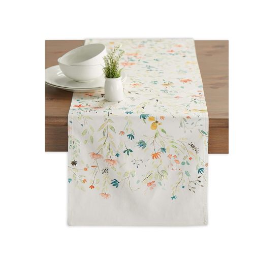 Floral table runner on a table with dishes on top.