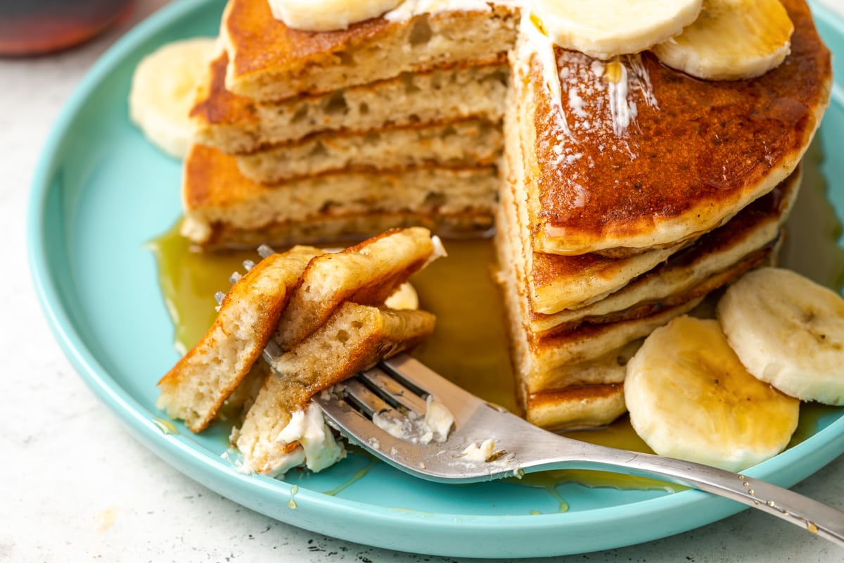 How to make banana pancakes - stacked and served with syrup with a bite missing.