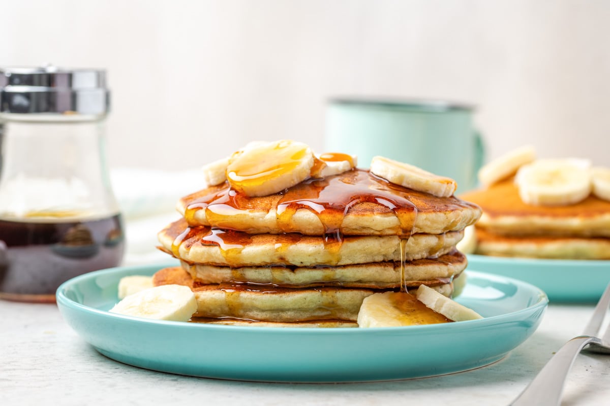 How to make banana pancakes - A stack of Banana Pancakes topped with syrup and bananas.