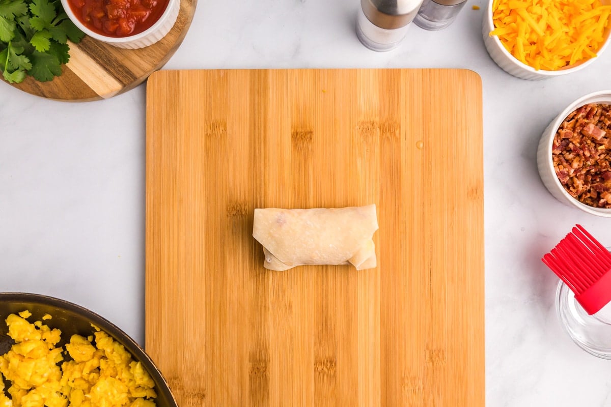 A filled egg roll on a cutting board.