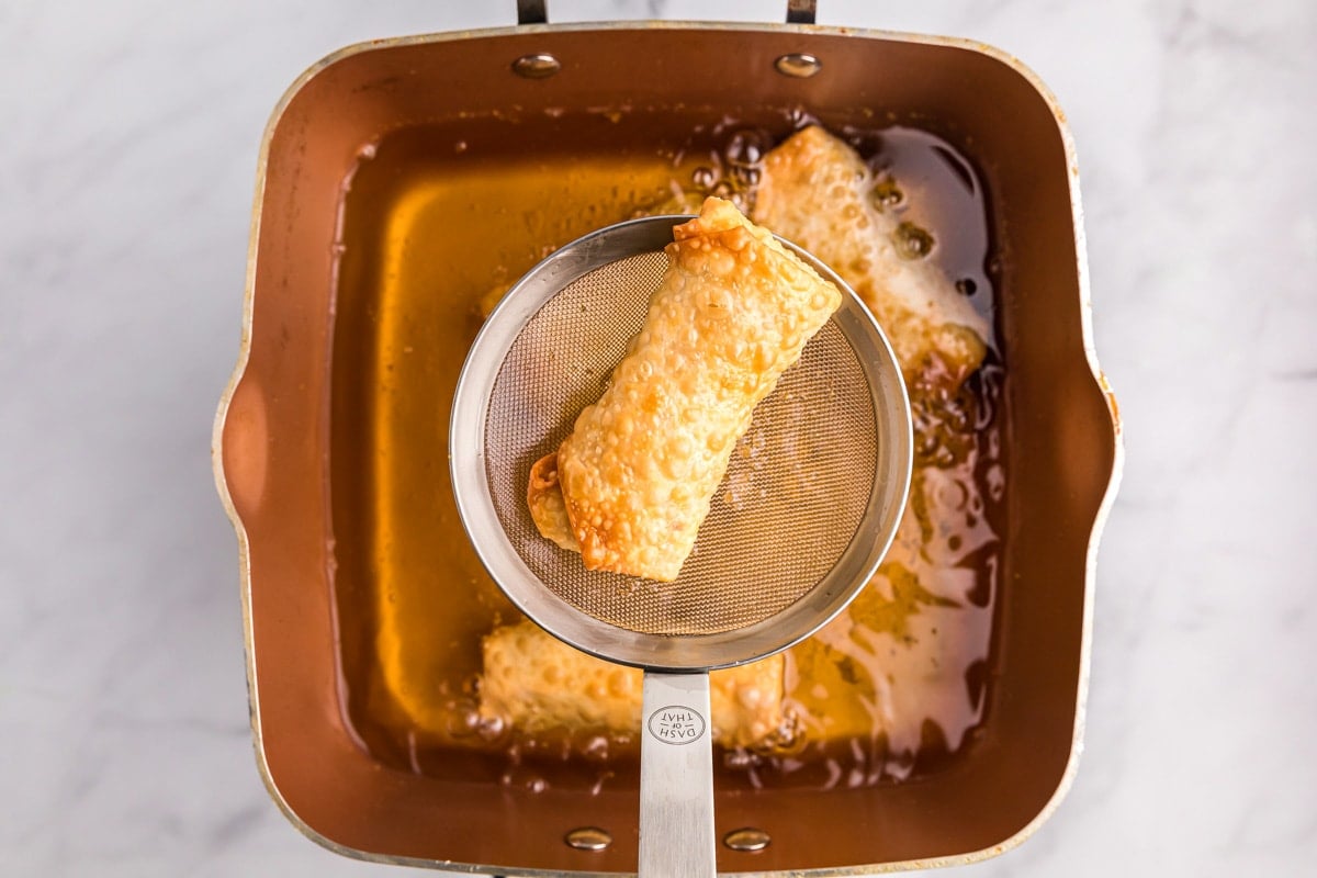 A fried breakfast egg roll in a mesh strainer above a pot of oil.