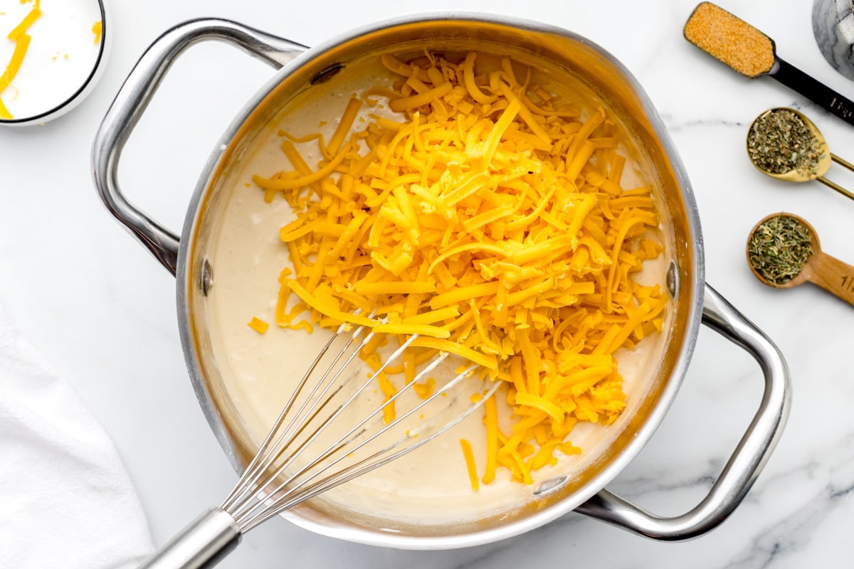 Adding shredded cheese to a pot full of sauce.