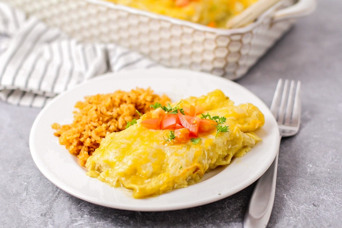 Green Chile Chicken Enchiladas in a 9x13 pan topped with tomatoes.