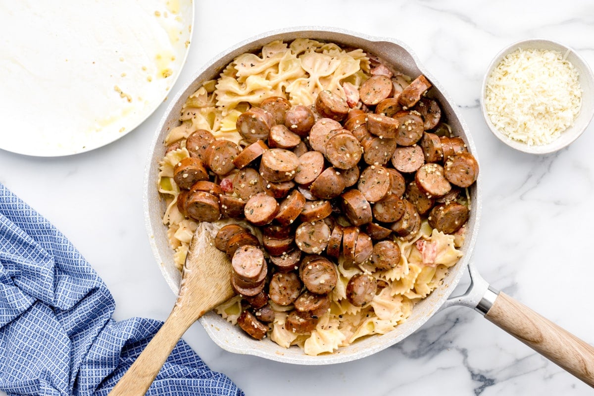 Mixing sausage into the pasta mixture in a skillet.