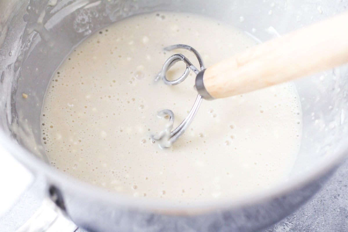 A metal bowl full of milk mixed with yeast with a Danish dough whisk in the bowl. 