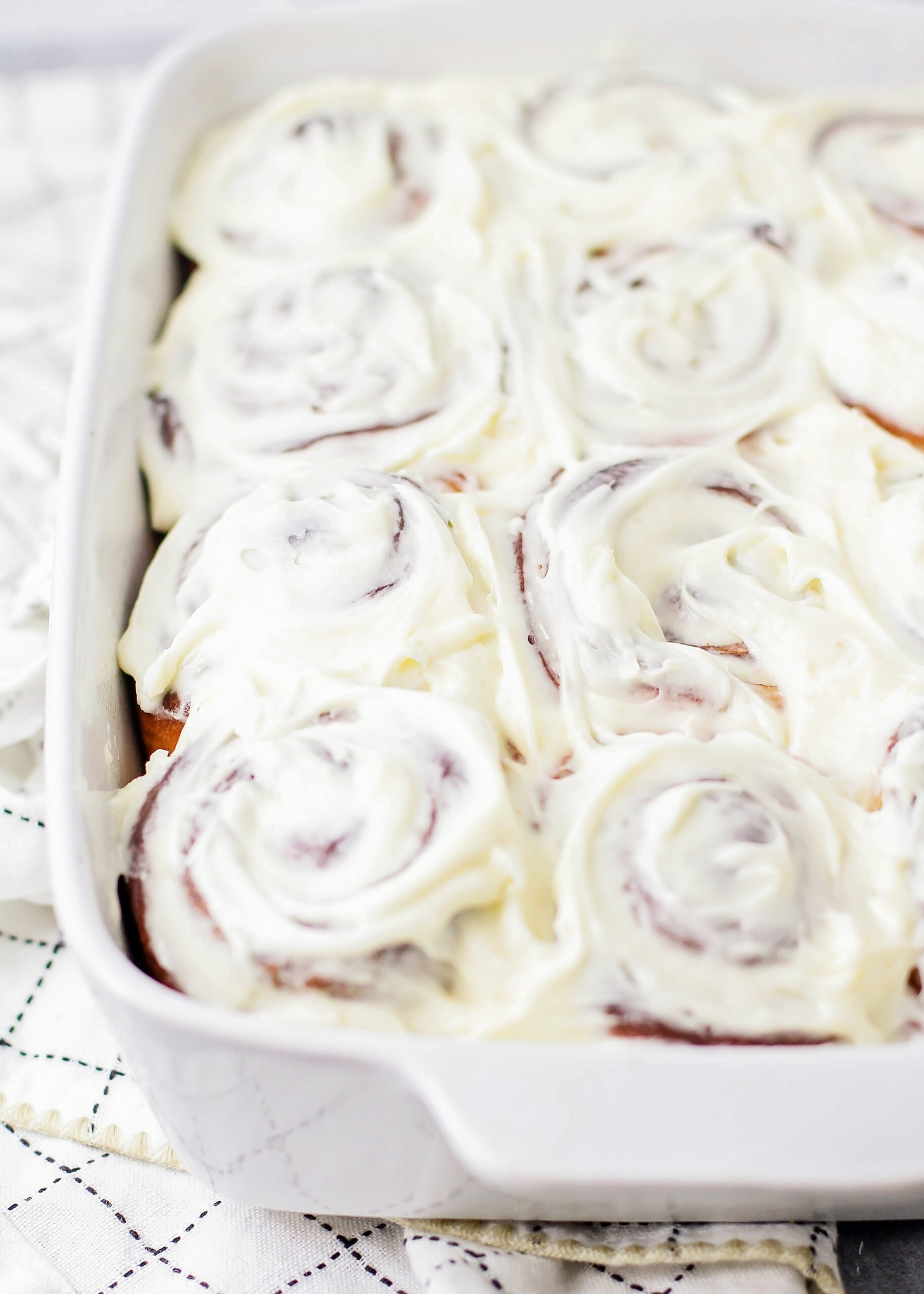 A white baking dish full of frosted homemade cinnamon rolls. 