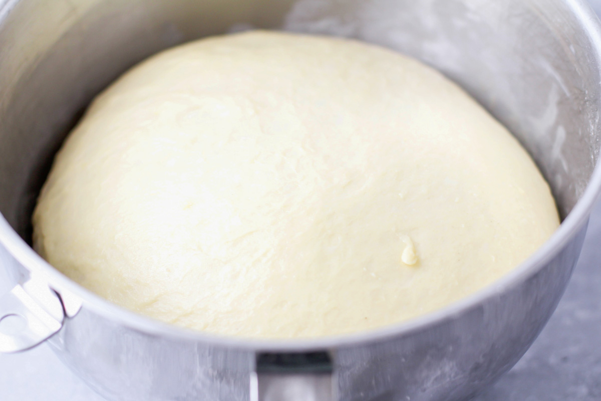 A metal bowl with cinnamon roll dough beginning to rise. 