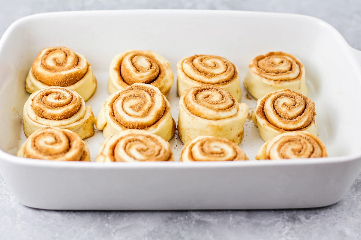 A white baking dish filled with a dozen cinnamon rolls ready to rise. 