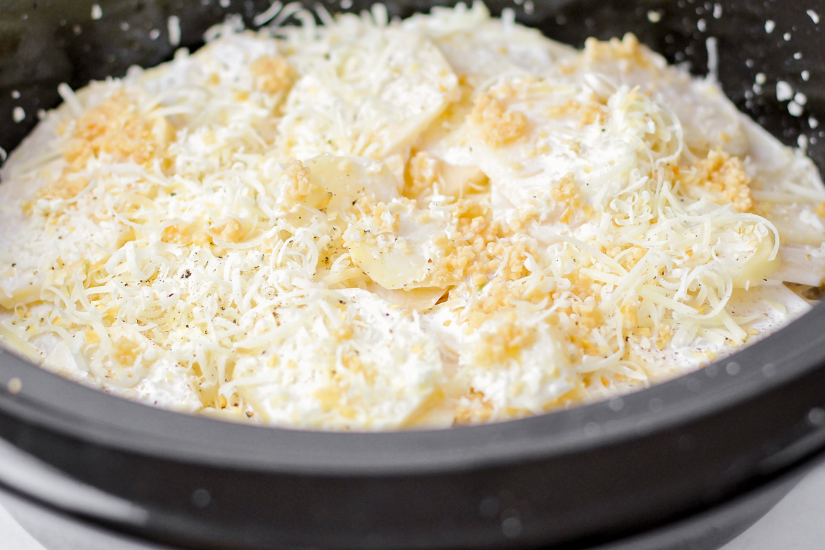 Cheese and garlic layered on top of potatoes in slow cooker.
