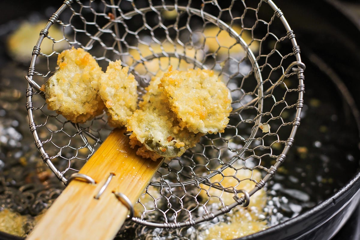 Frying pickles in a pan on the stove for deep fried pickles.