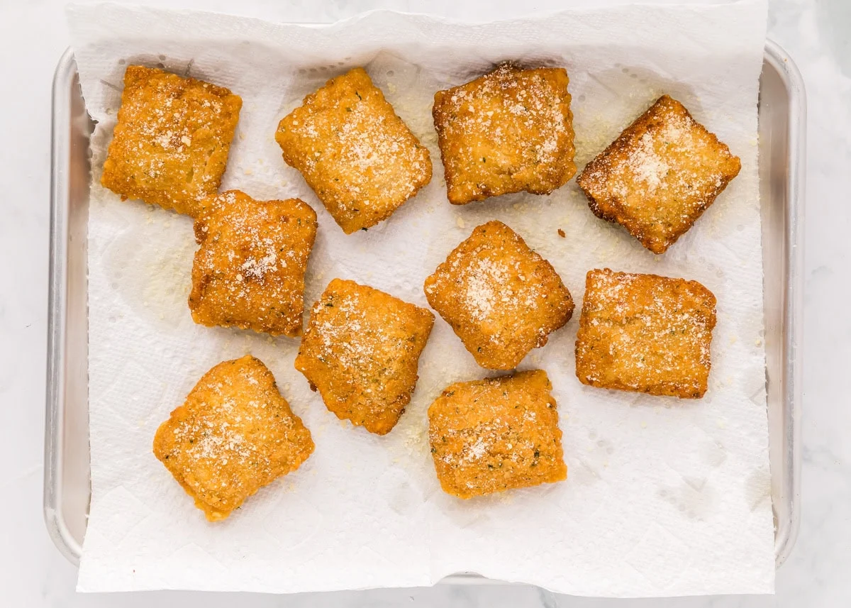 Fried ravioli draining on a paper-towel lined pan.