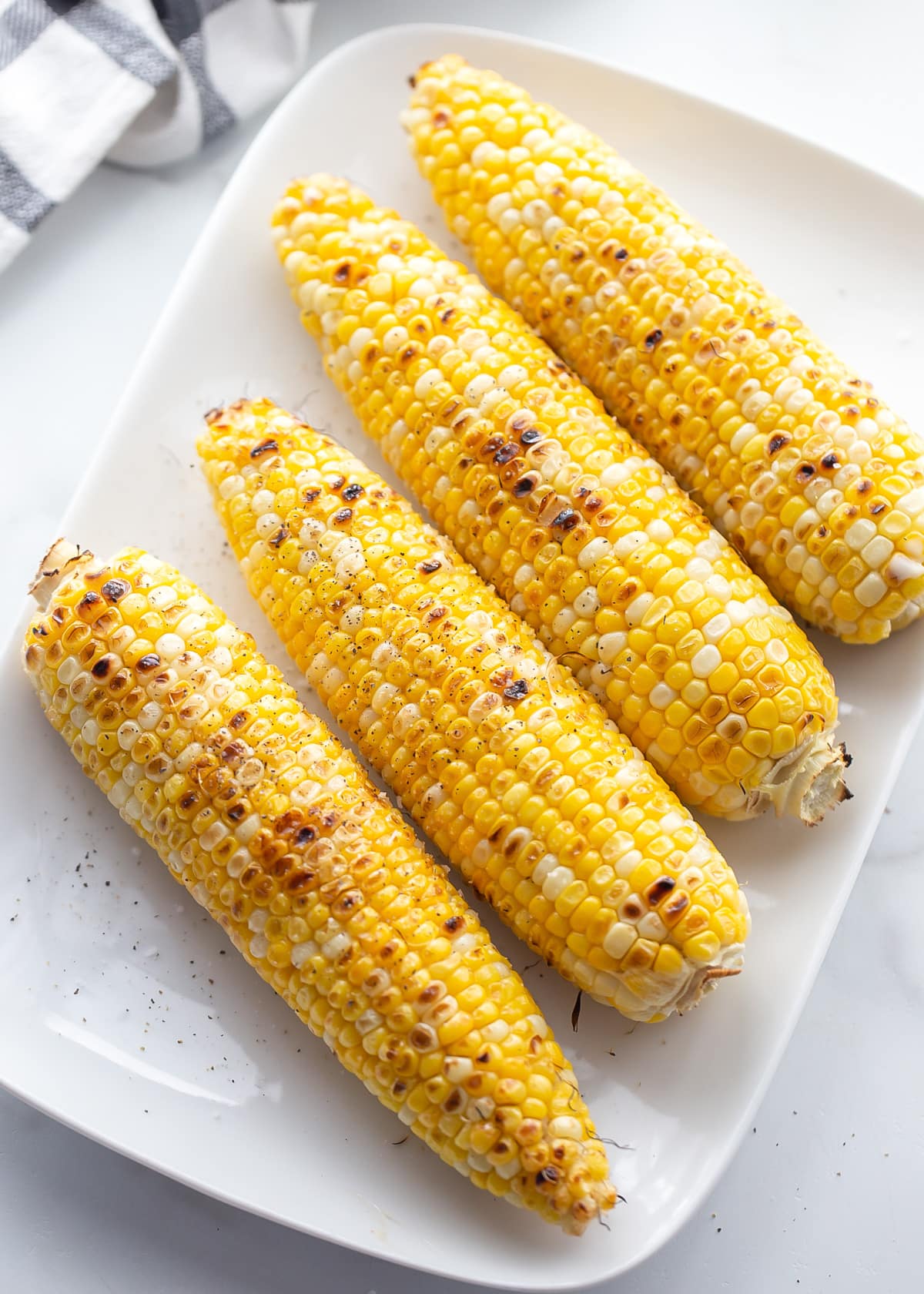 Seasoned grilled corn on the cob served on a white plate.