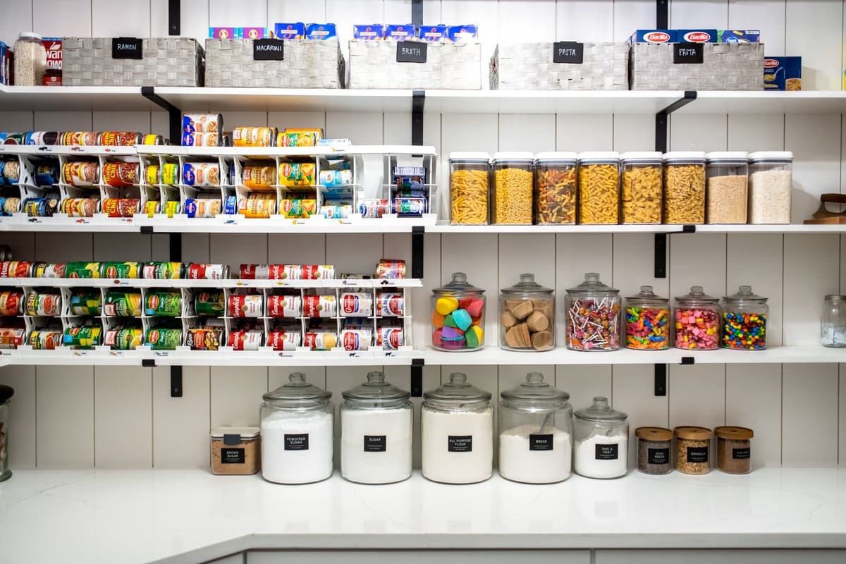 Pantry shelves filled with canned goods on can rotators, dried pasta in storage containers, and candy stored in glass jars.