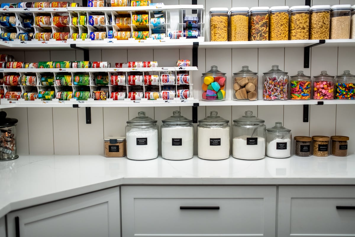 An organized pantry with can organizers, containers and jars lining the shelves.