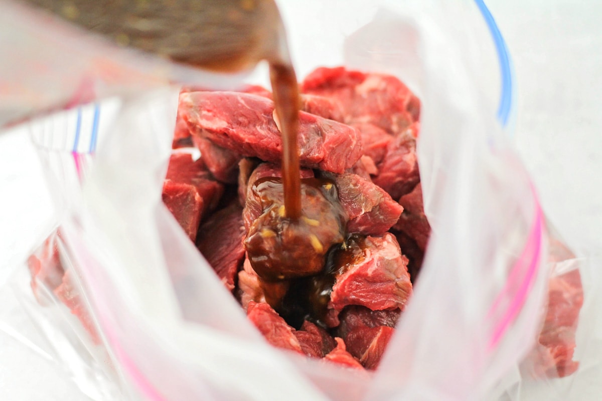 Pouring marinade over piece of meat in a ziploc bag.