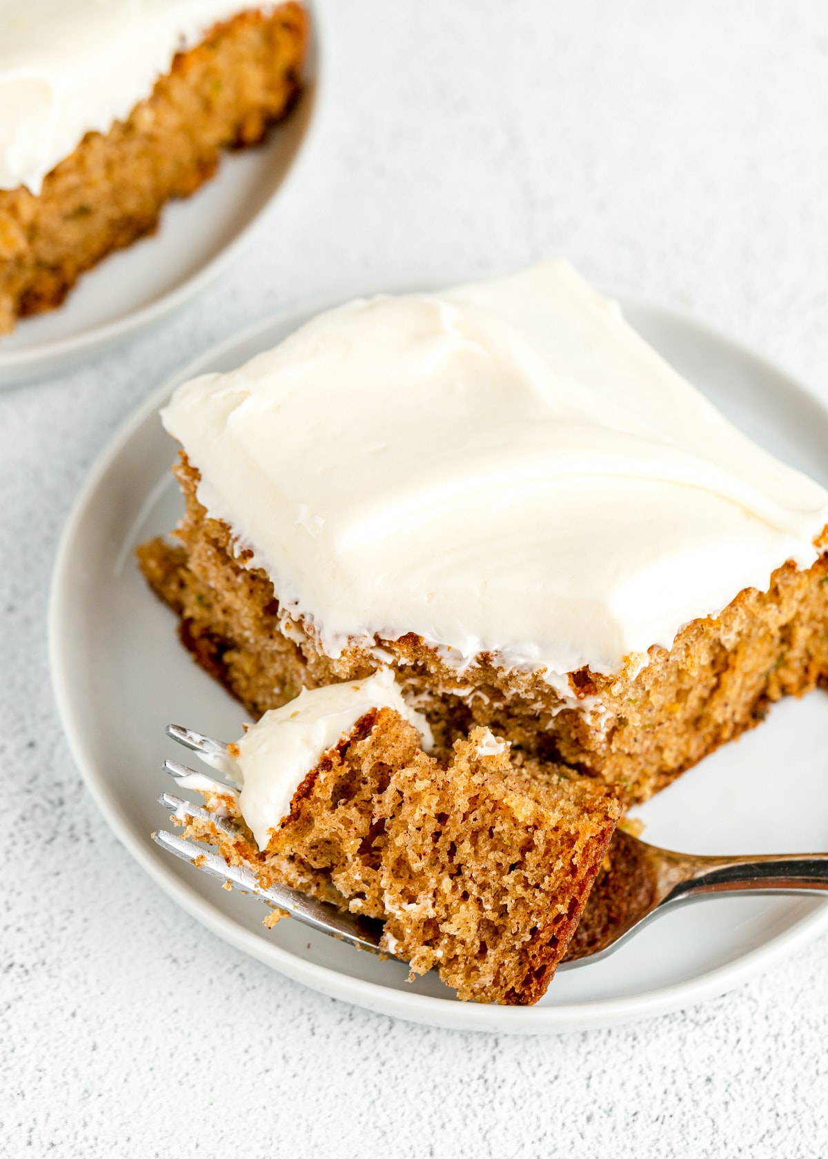 A fork full of a slice of zucchini cake topped with cream cheese frosting.