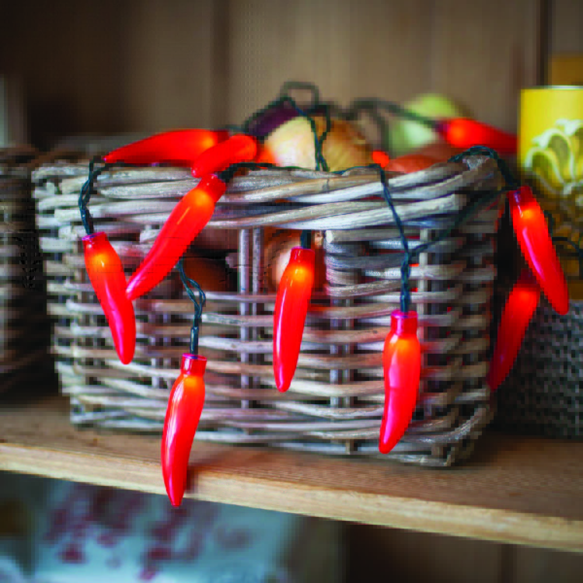 A rectangular basket with red chili pepper lights hanging out of it sitting on a wooden shelf.