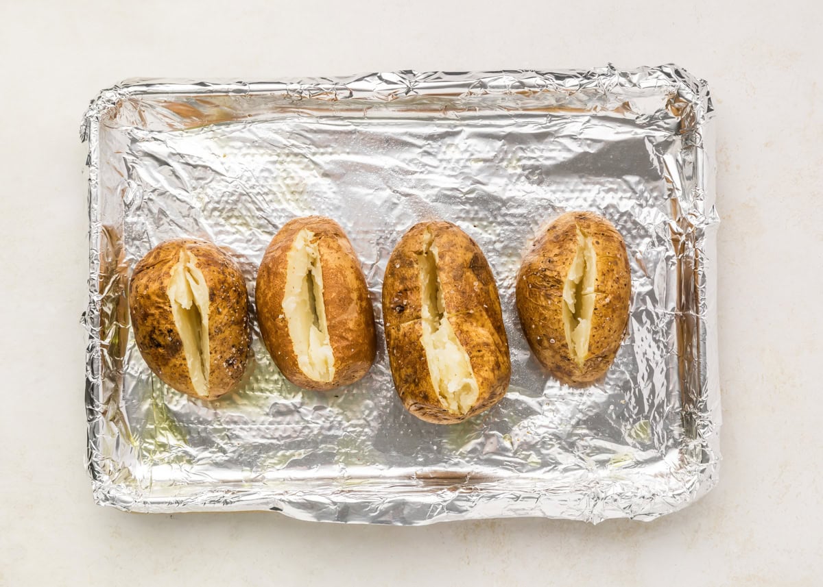 Perfect baked potatoes on foil lined baking sheet cut open.