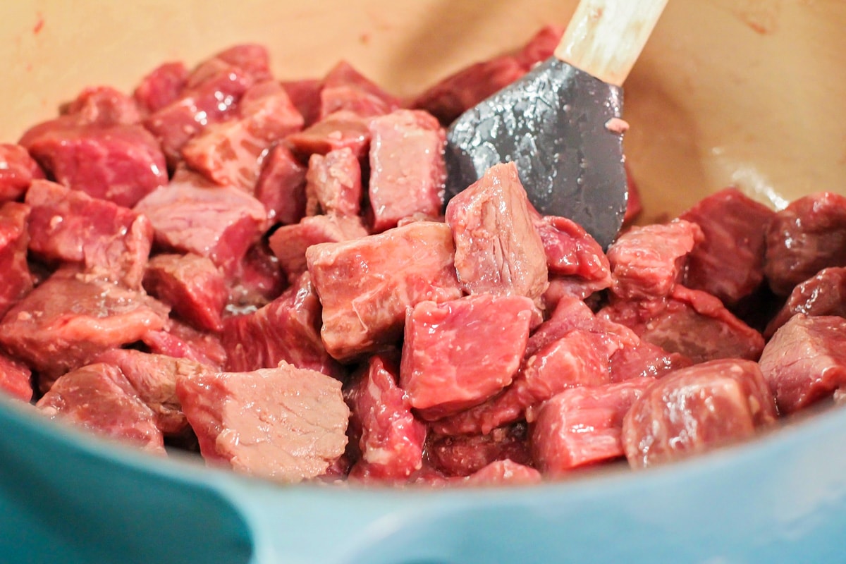 Raw beef cubes cooking in a Dutch oven pot.