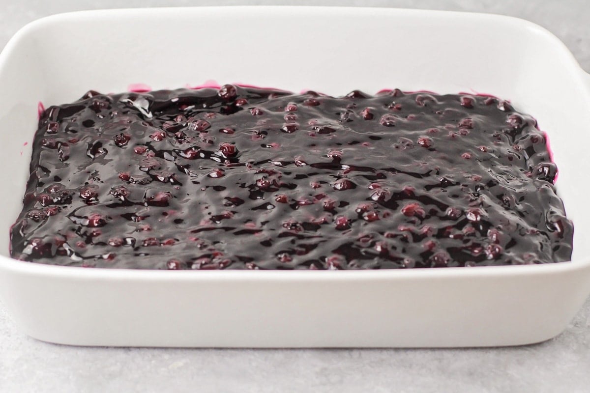 Spreading the blueberry filling into the bottom of the white baking dish.