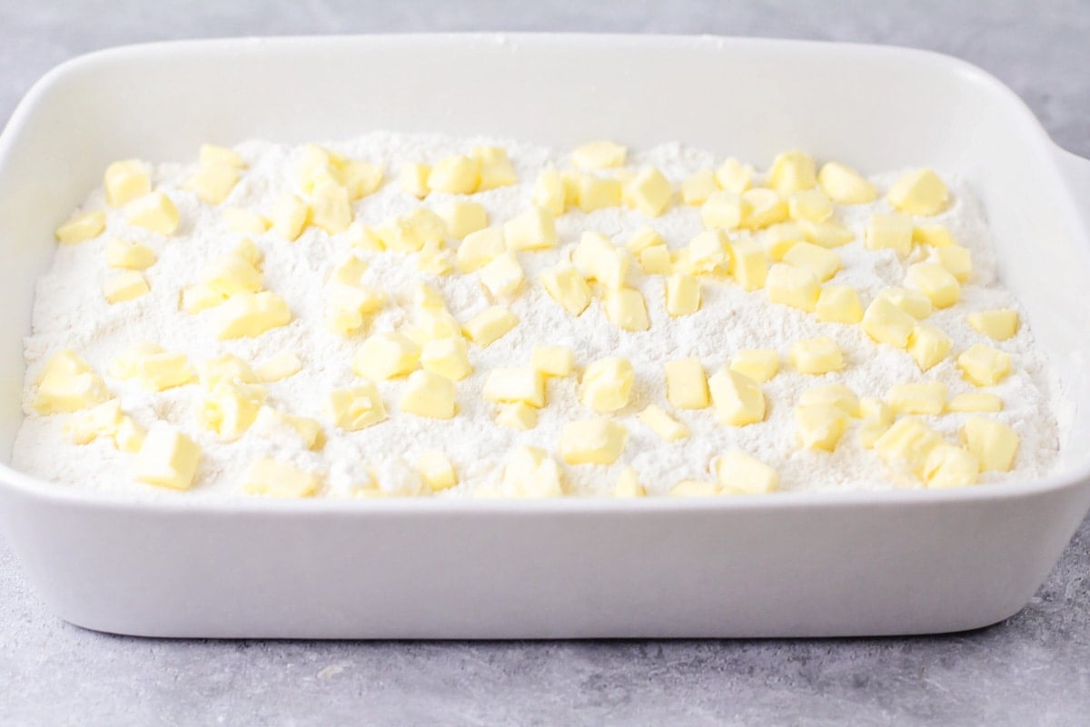 Butter chunks on top of a cake mix layer in a baking dish.
