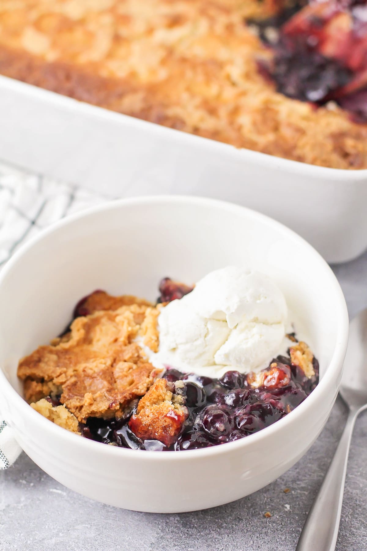 Blueberry dump cake scooped into a white bowl and served with a scoop of vanilla ice cream.