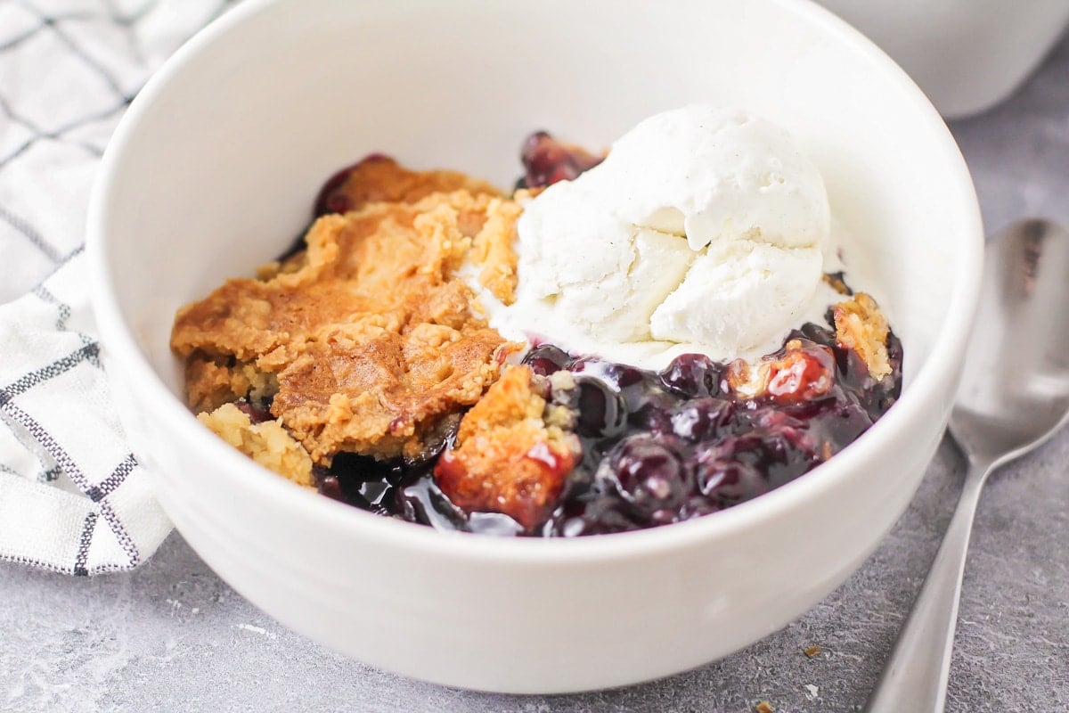 A scoop of blueberry dump cake in a white bowl with a scoop of vanilla ice cream.