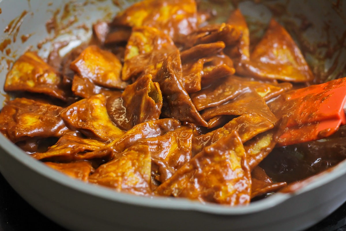 Covering tortilla chips with red enchilada sauce in a pan.