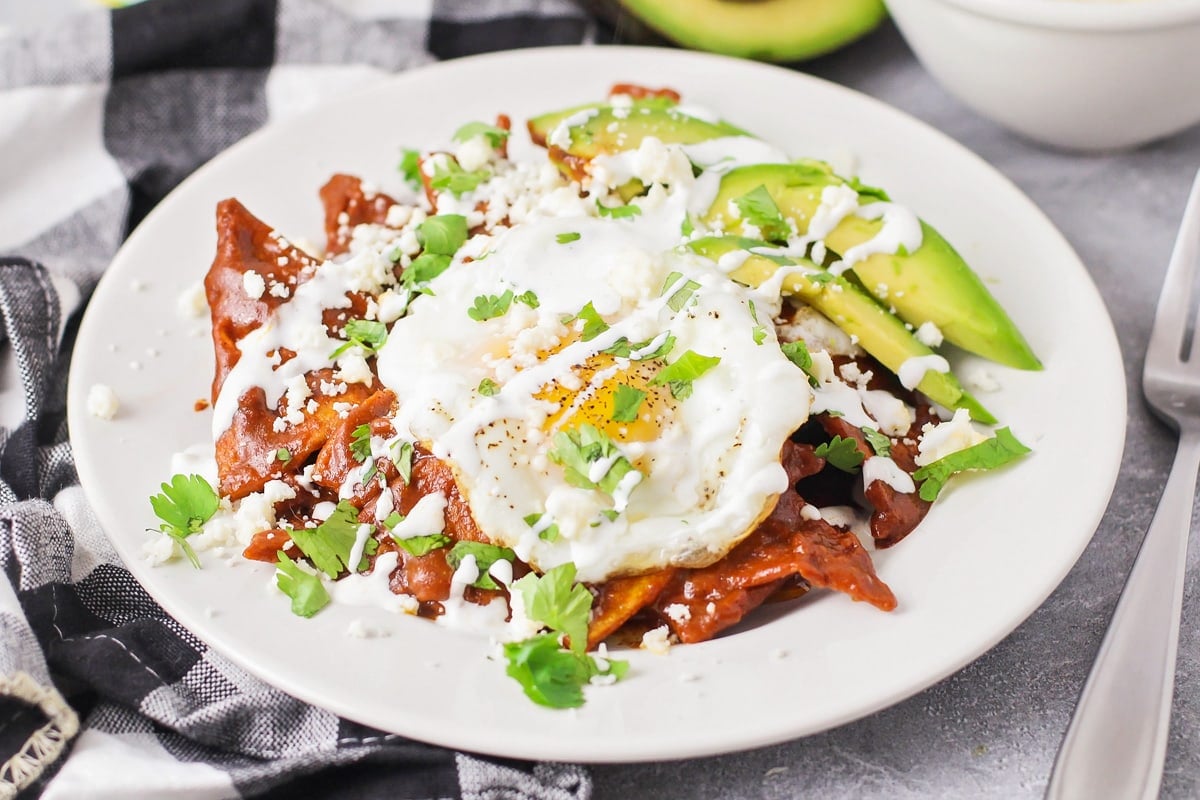 How to make chilaquiles tutorial - A plate of chilaquiles topped with a fried egg, avocado, and cotija.