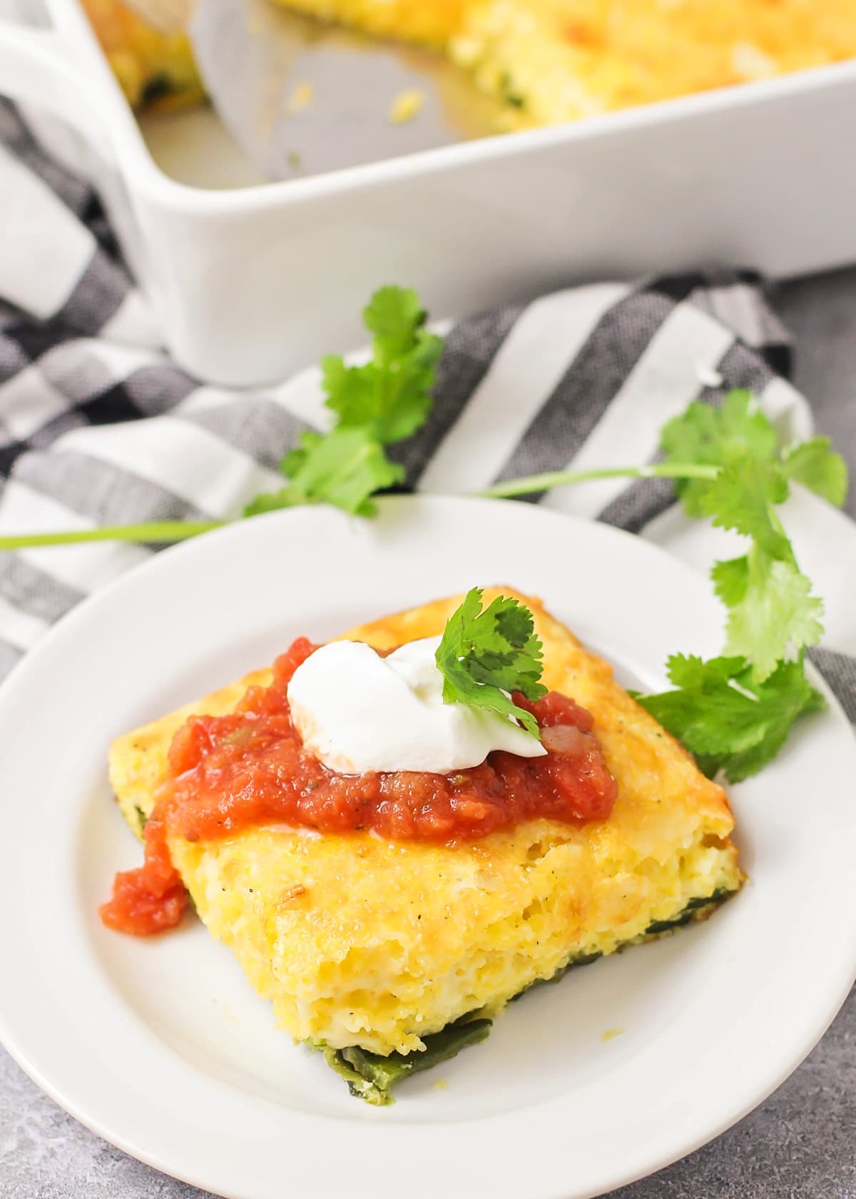 A square slice of chile relleno casserole topped with sour cream and salsa.