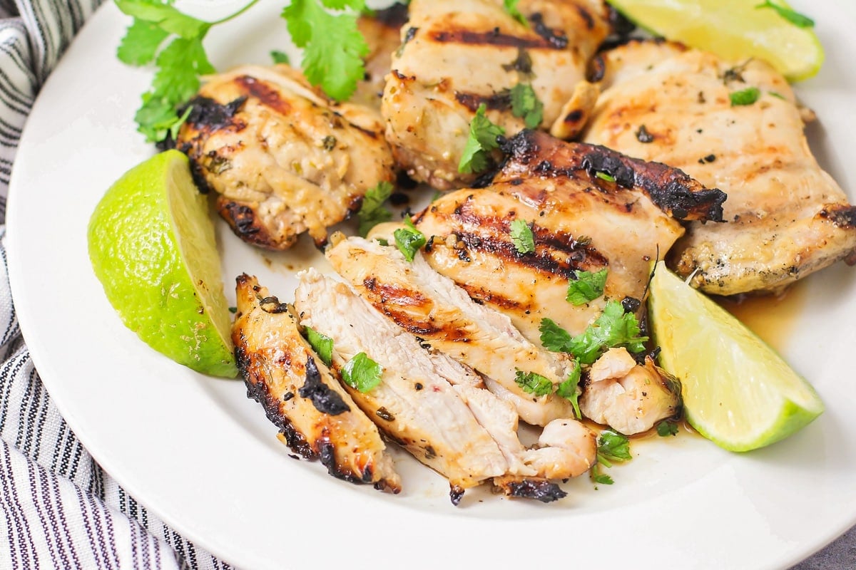 Grilled cilantro lime chicken on a plate with sliced limes.