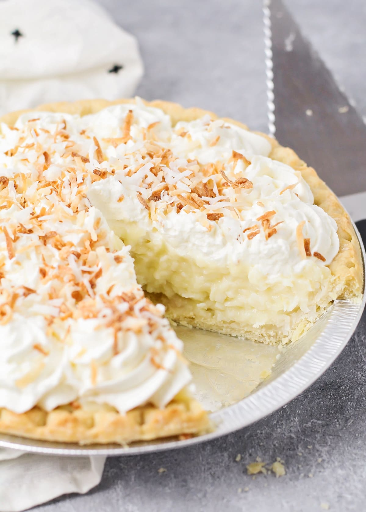 A close up of a coconut cream pie with one slice missing.