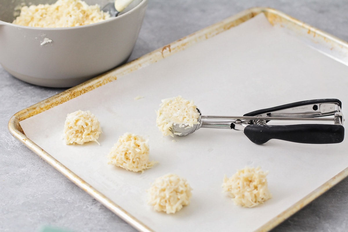 Scooping coconut mixture onto a  lined baking sheet with an ice cream scoop.