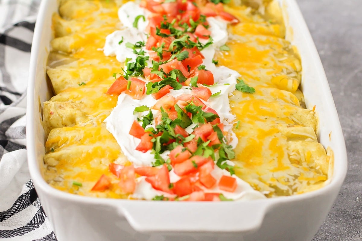 A dish of cream cheese chicken enchiladas topped with sour cream, diced tomatoes, and fresh cilantro.