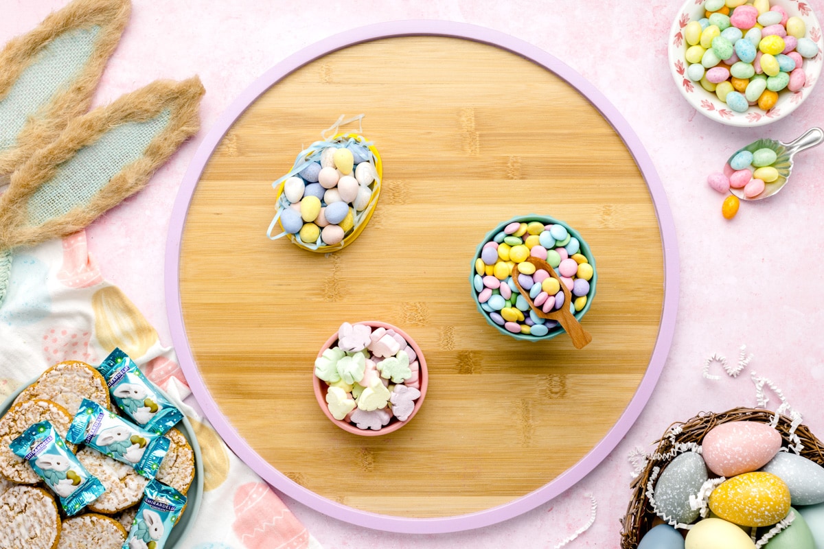 Three small bowls filled with Easter candy on a wooden platter.